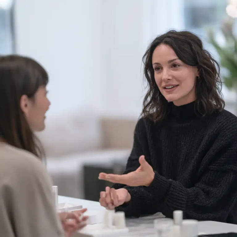 Prothésiste ongulaire en conversation avec une cliente autour d’une table : le parrainage en onglerie se propose de vive voix, en fin de rendez-vous.