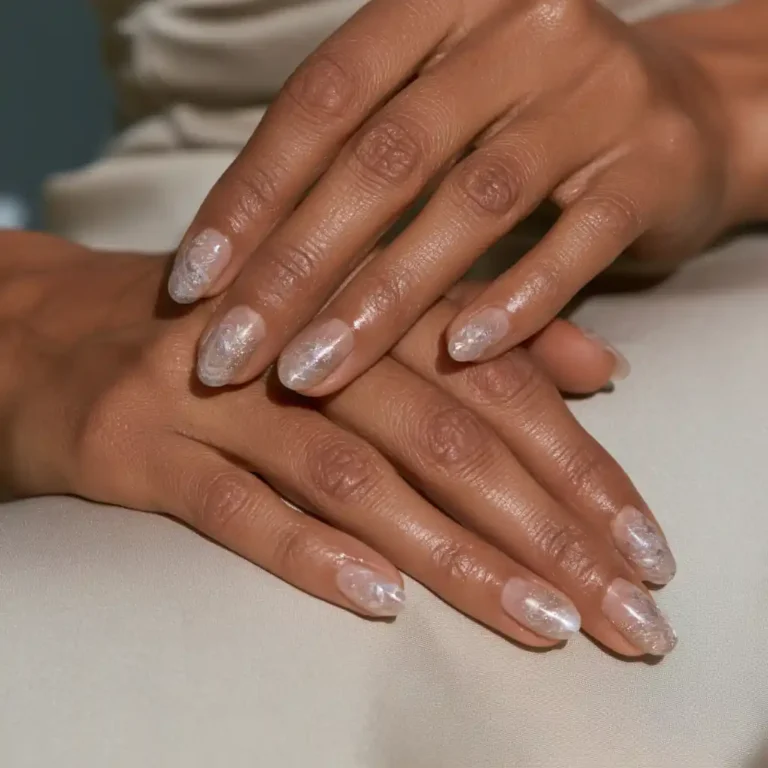 Ongles ovales nacrés et brillants, décorés de motifs blancs irisés : le rendu d’une finition top coat